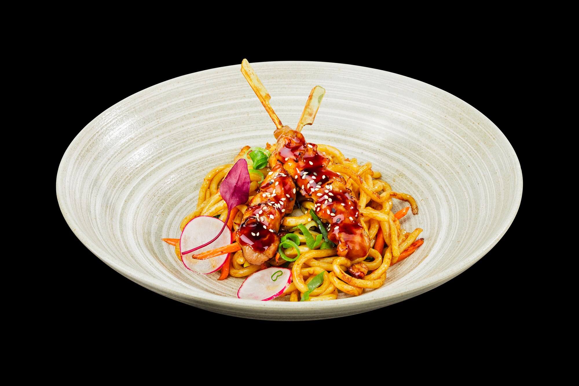 Pasta und Hühnchen am Spieß vor schwarzem Hintergrund