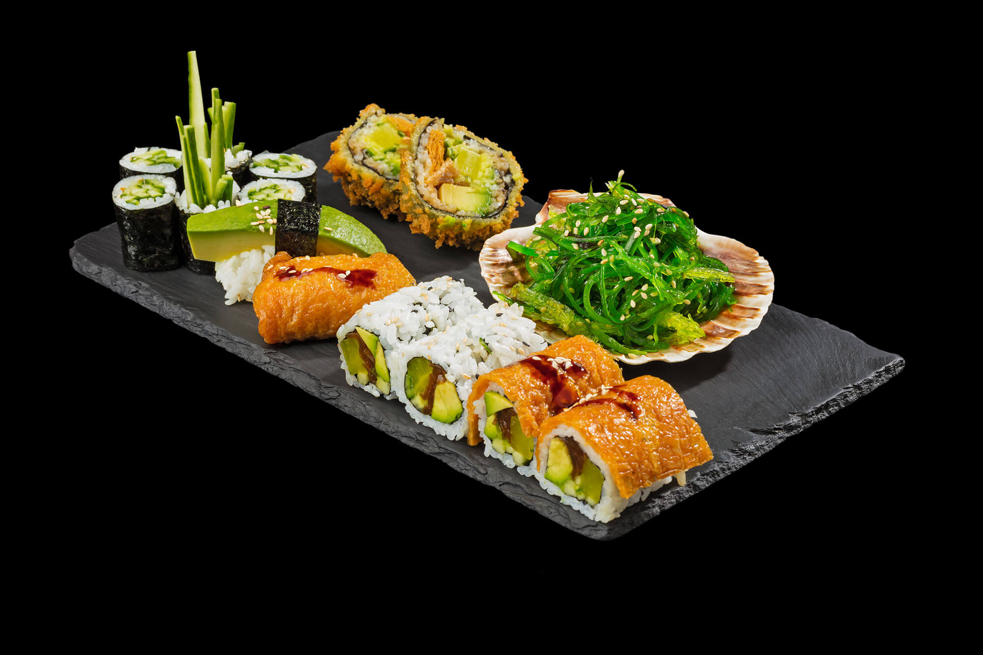 Sushi Platte und Algensalat auf Schieferplatte vor schwarzem Hintergrund