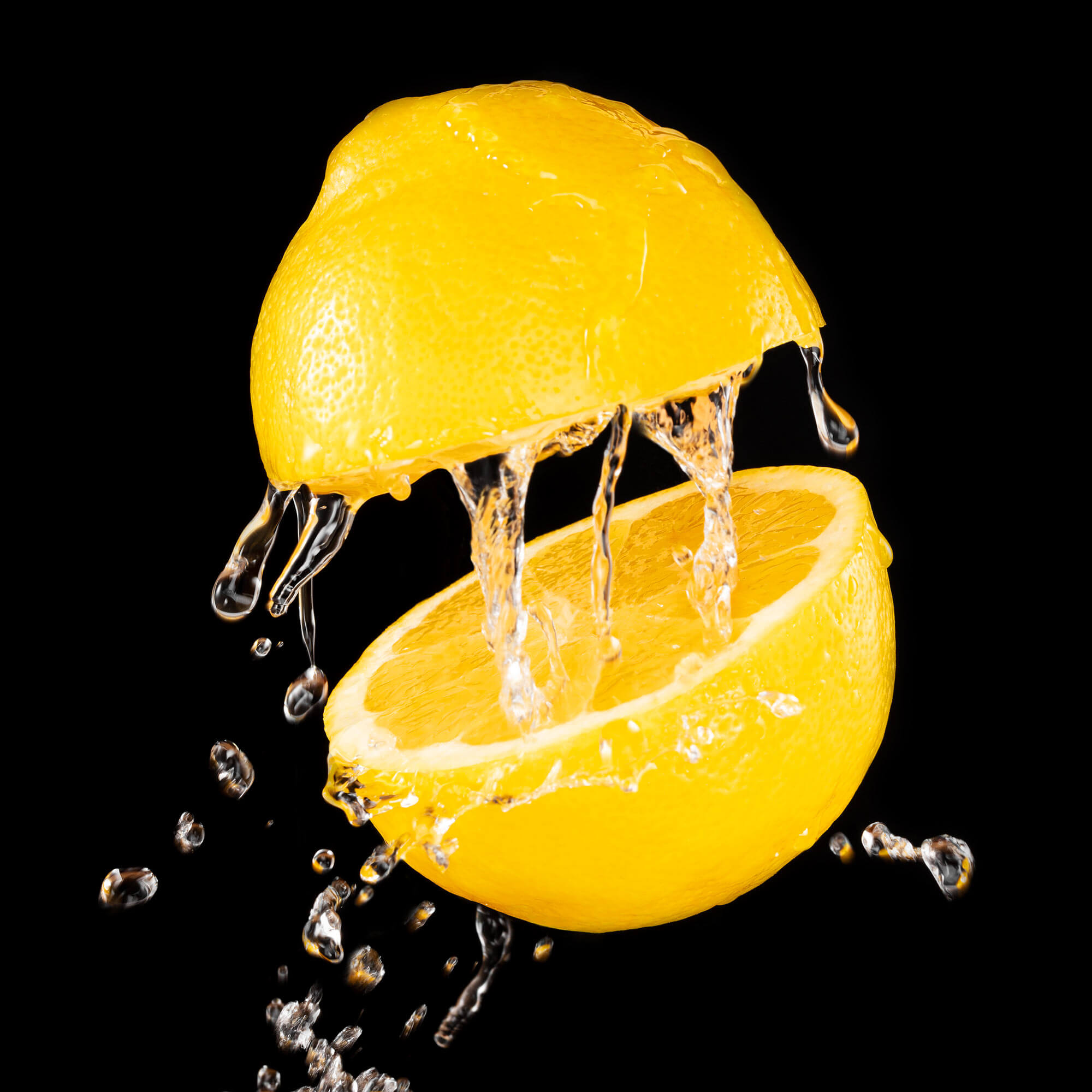 Zitrone mit Wasserspritzern vor schwarzem Hintergrund