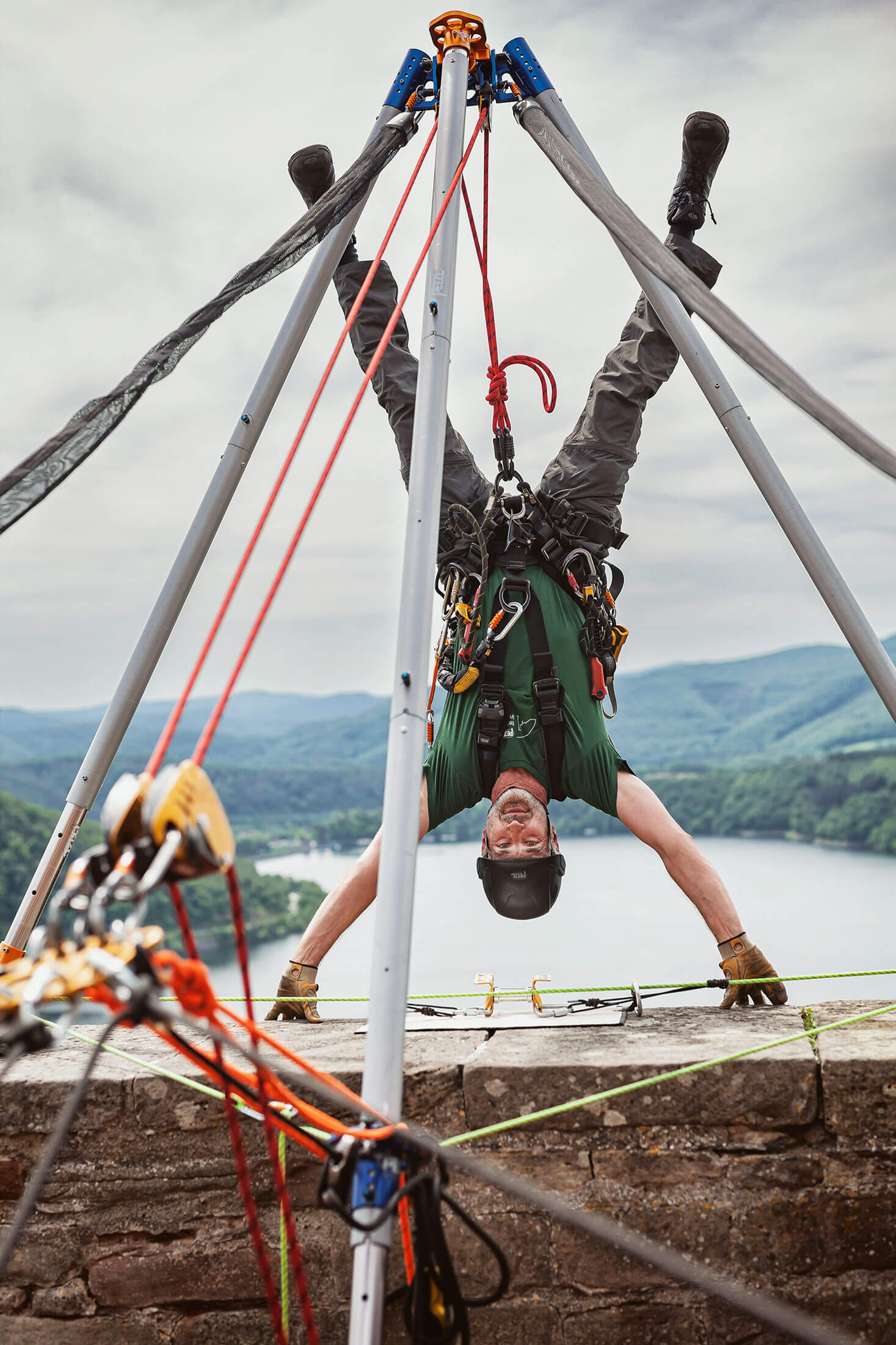 Mann hängt gesichert an einem Seil kopfüber an einem Abgrund