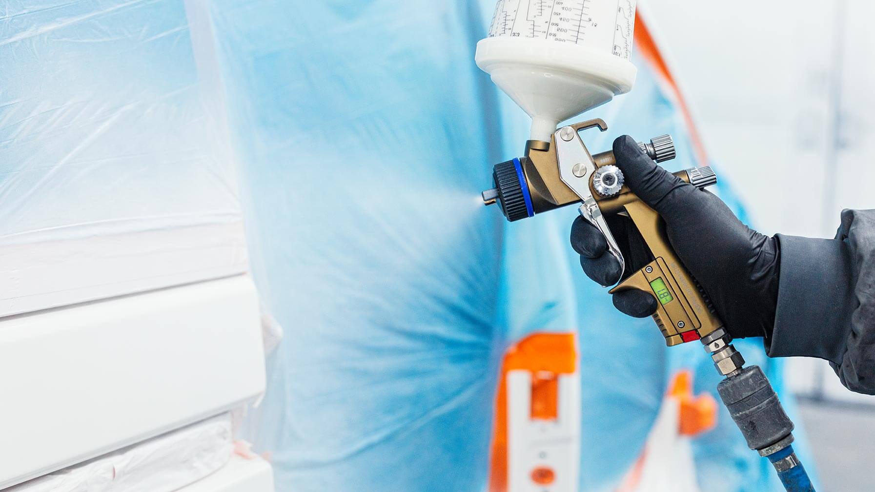 Mann lackiert mit Lackierpistole ein Auto in einer Lackierkabine