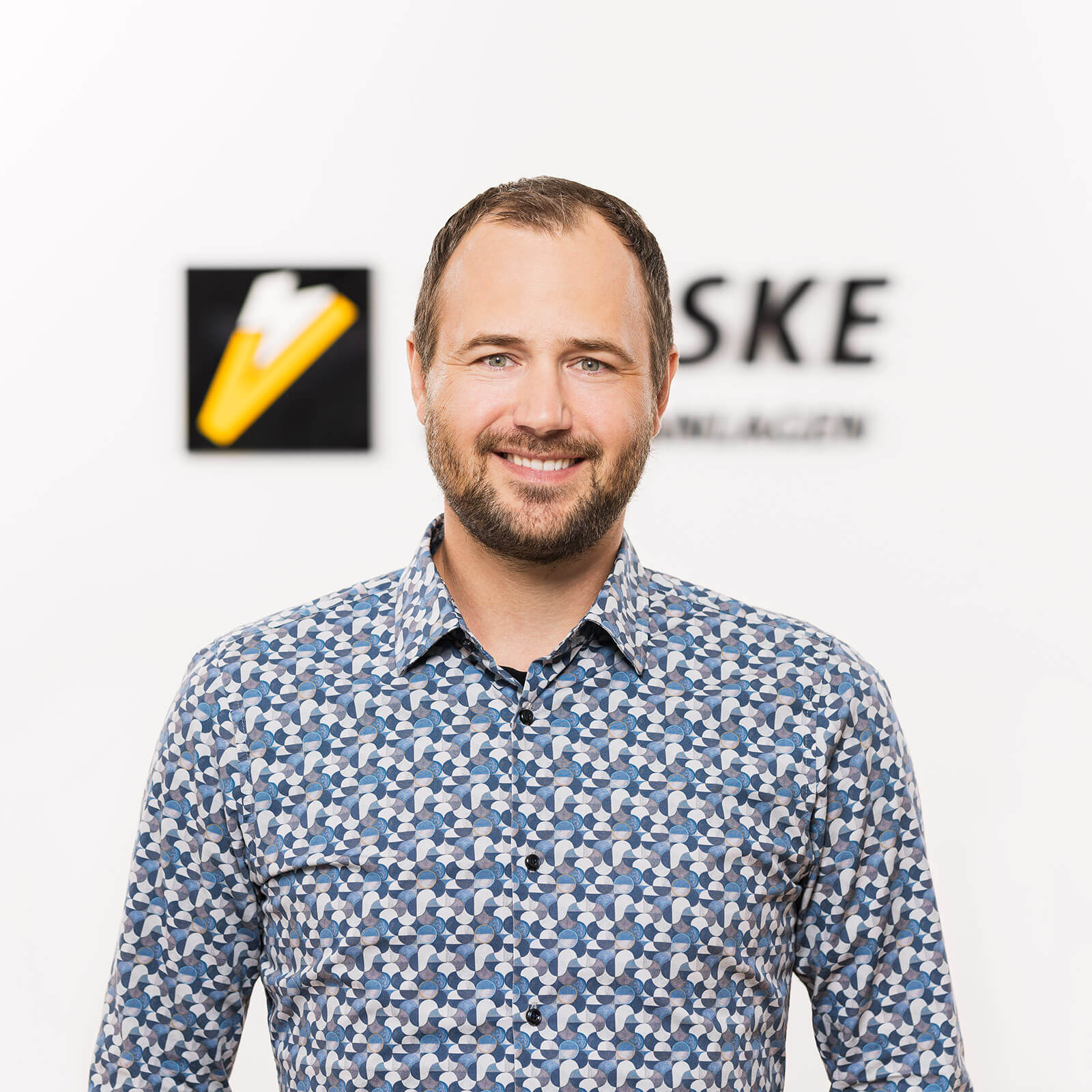 Businessportrait Mitarbeiter vor Firmenlogo