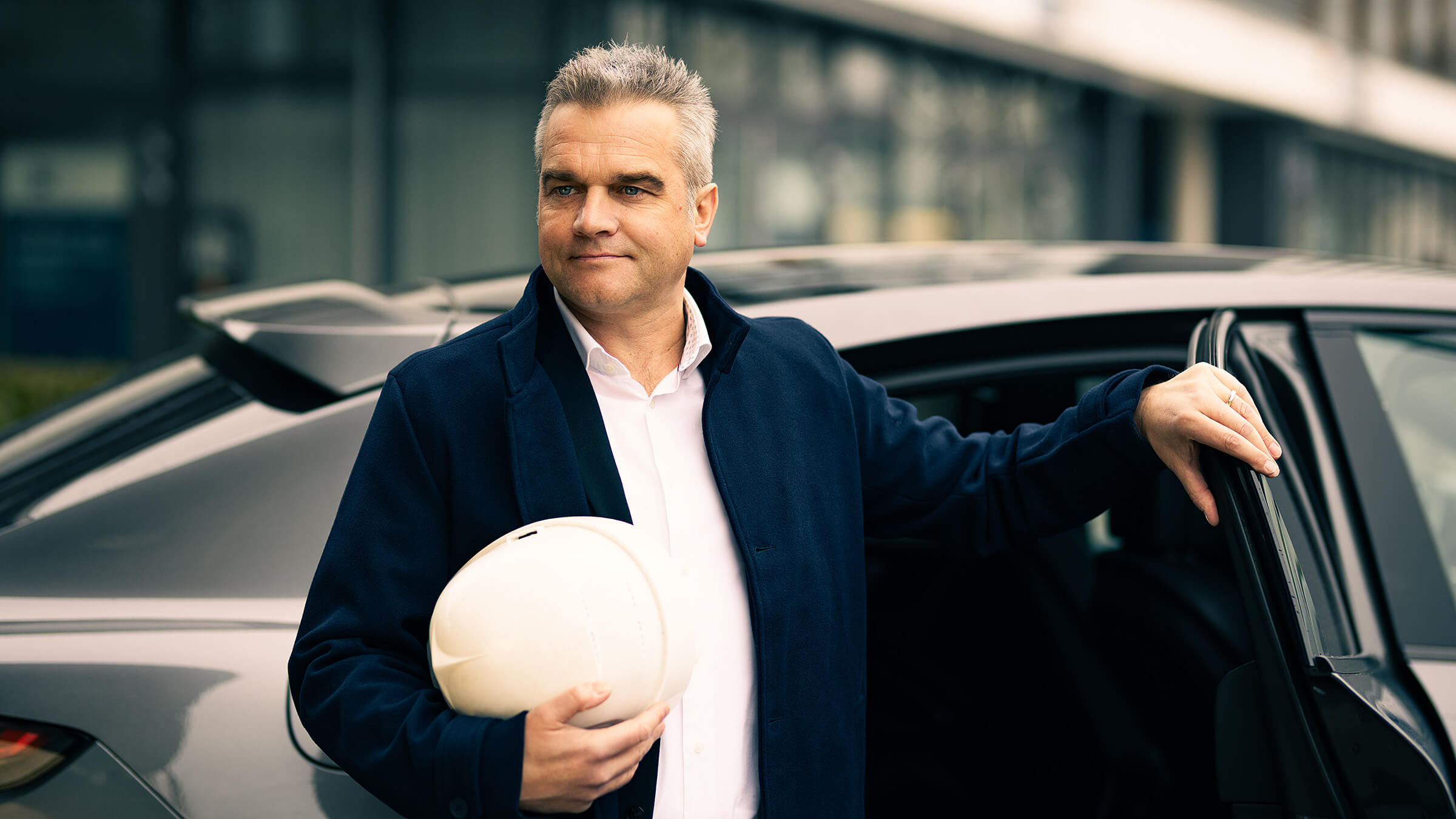 Mann vor Auto mit Gebäude im Hintergrund