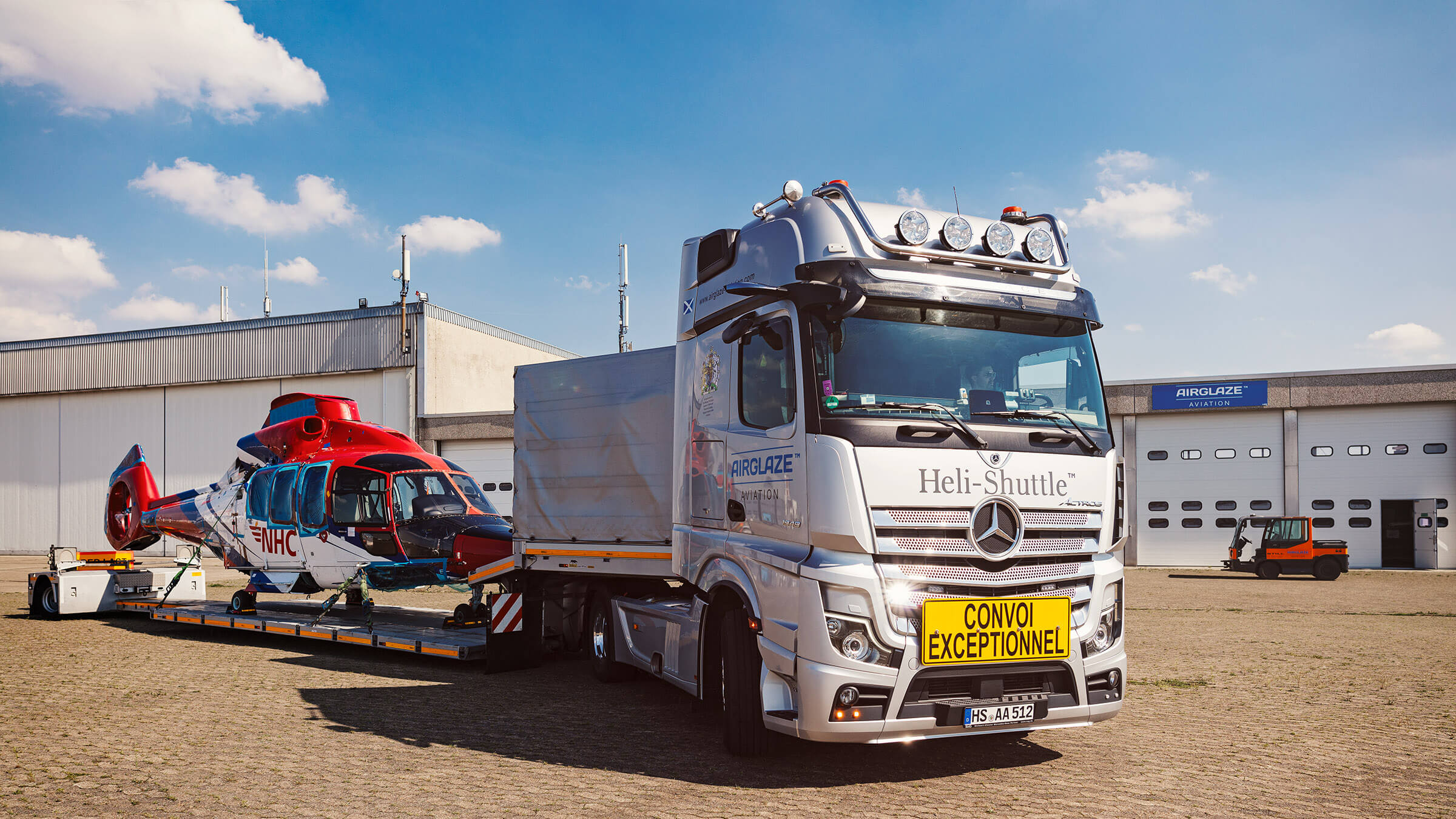 Hubschrauber Transport auf LKW vor Hangar und blauem Himmel