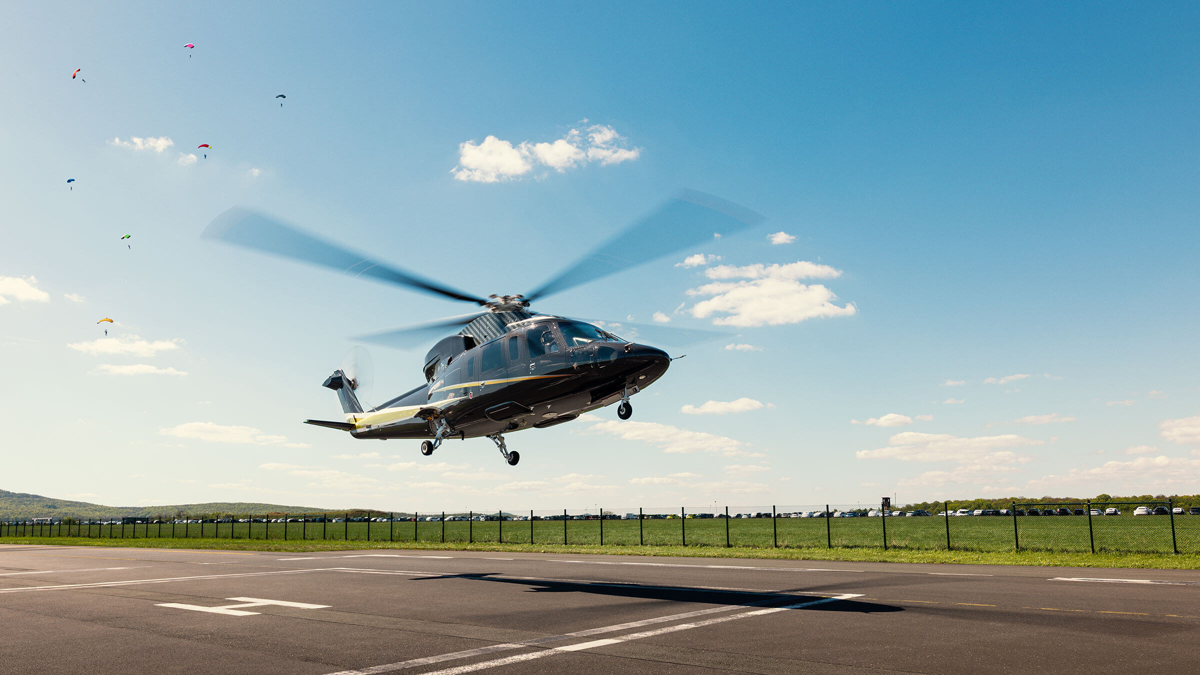 Hubschrauber beim Start auf Flugplatz mit Fallschirmspringern im Hintergrund