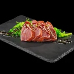 Thunfisch auf einem schwarzen Teller vor schwarzem Hintergrund.