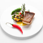 Gebratenes Fischfilet mit Gemüse und Beilagen auf einem weißen Teller.