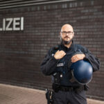 Polizist in Uniform mit Schutzhelm vor einer dunklen Gebäudewand.