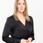 Businessportrait einer Frau mit langen blonden Haaren und schwarzem Oberteil vor hellem Hintergrund.