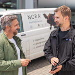 Zwei Männer im Gespräch vor einem Firmengebäude während einer authentischen Businessaufnahme.