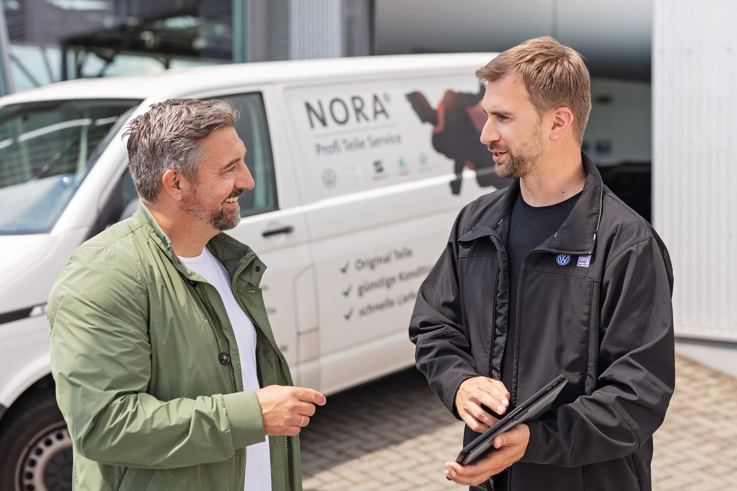 Zwei Männer im Gespräch vor einem Firmengebäude während einer authentischen Businessaufnahme.