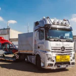 Hubschrauber wird bei Sonnenschein vor einem Hangar auf einen Lkw verladen