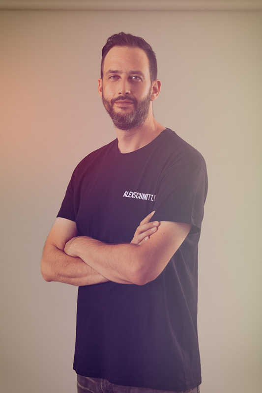 Portrait eines Mannes mit Bart und verschr&auml;nkten Armen vor einem warmen Hintergrund.