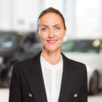 Professionelles Portrait einer Mitarbeiterin im Business-Look vor einem hellen, modernen Hintergrund.
